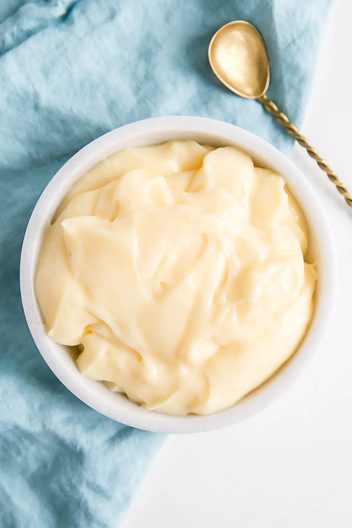 Pastry cream in a bowl with a gold spoon beside it.