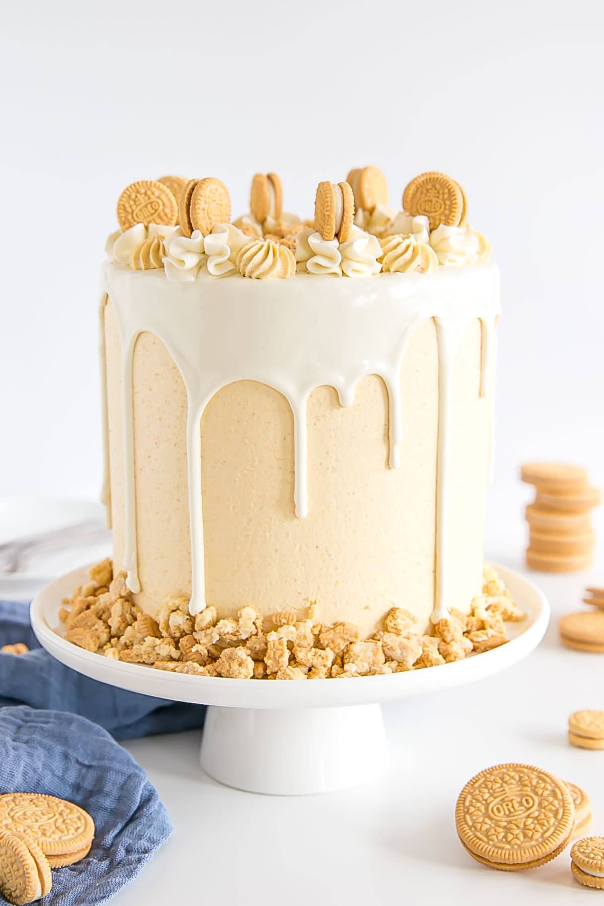 Golden Oreo cake on a white cake stand. Decorated with a white chocolate ganache drip and rosettes on top.