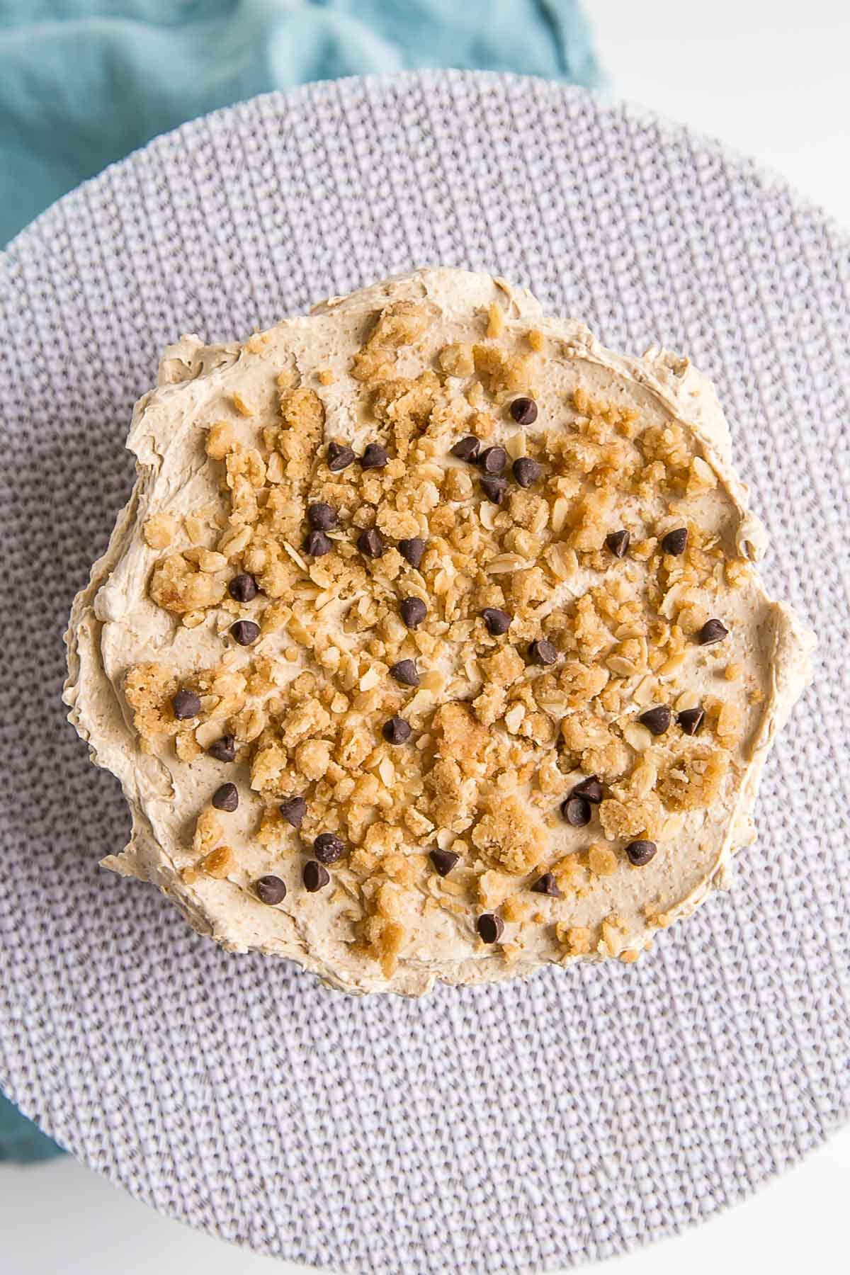 Frosted cake layer on a turn table showing sprinkled cookie crumble and chocolate chips.