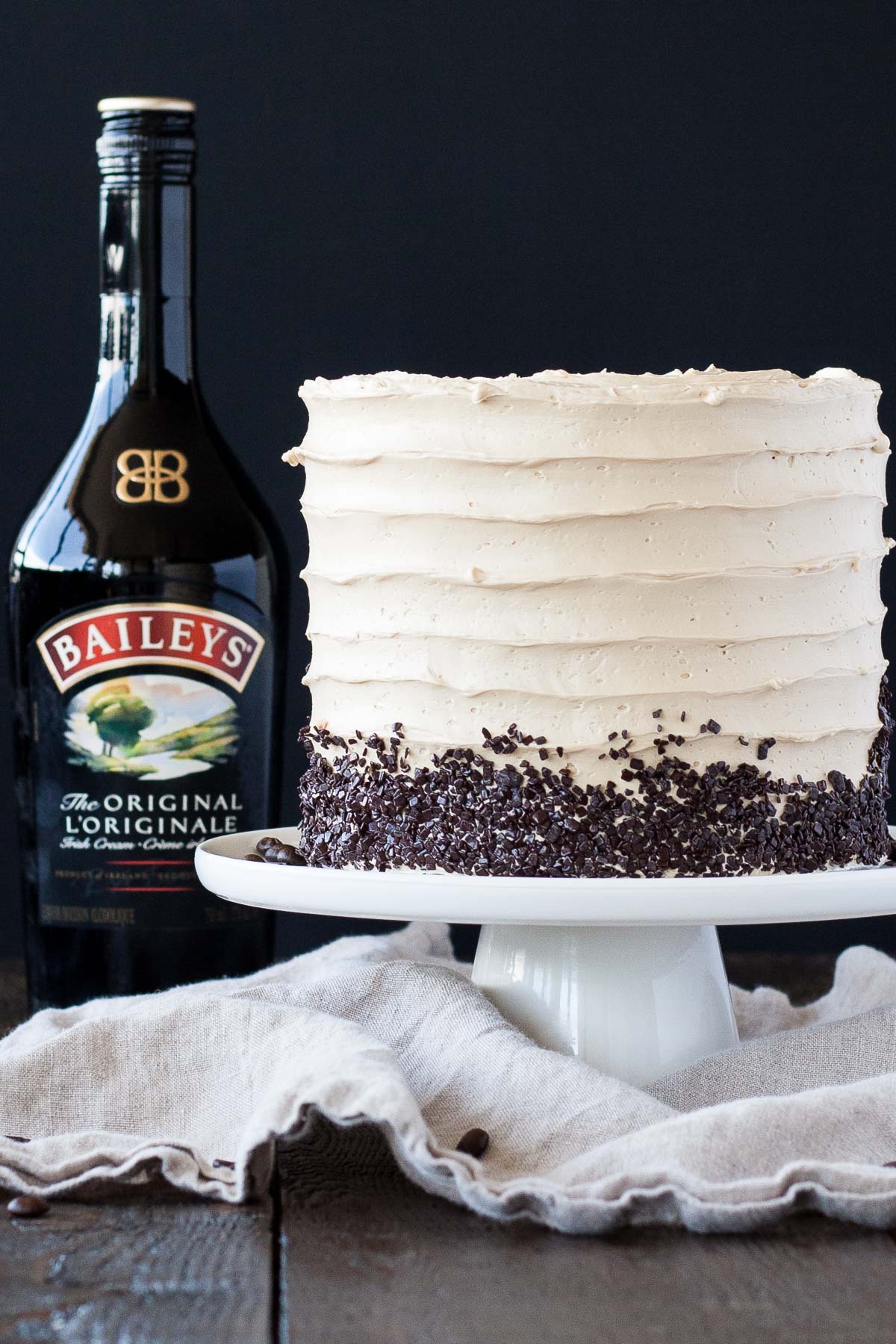 Cake on a white cake stand with a bottle of Baileys behind it.