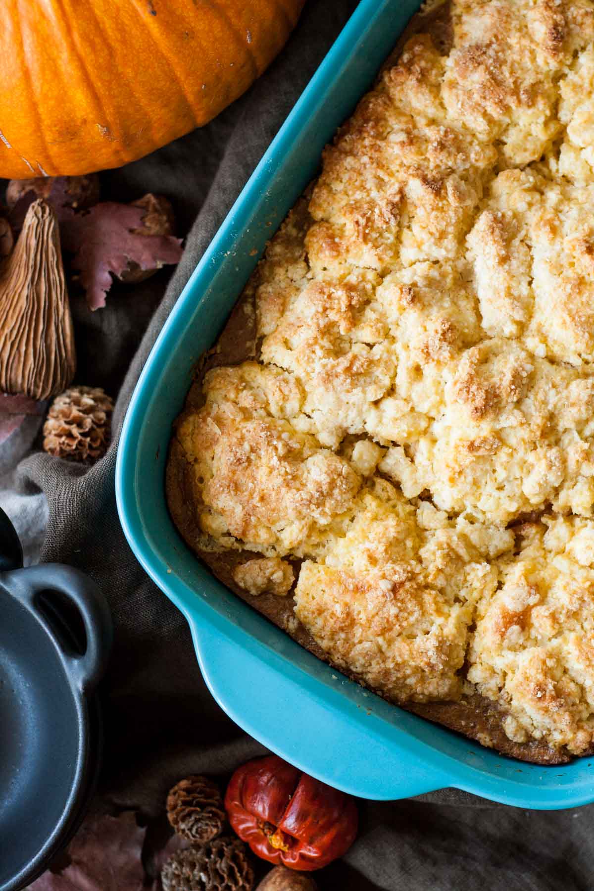 Overhead shot of pumpkin cobbler in a teal casserole dish with fall decor around it.