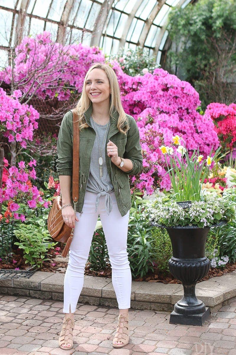 A neutral spring look with white jeans, sandals, and a green jacket.