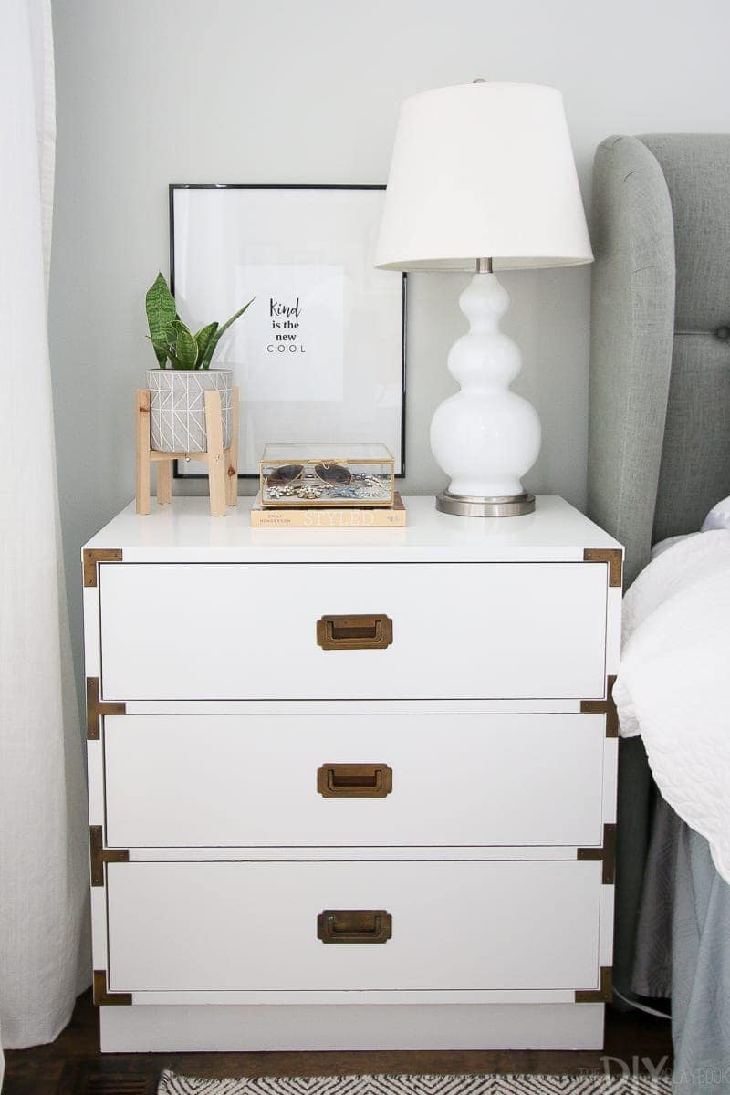 A white campaign style nightstand decorated in this master bedroom. 