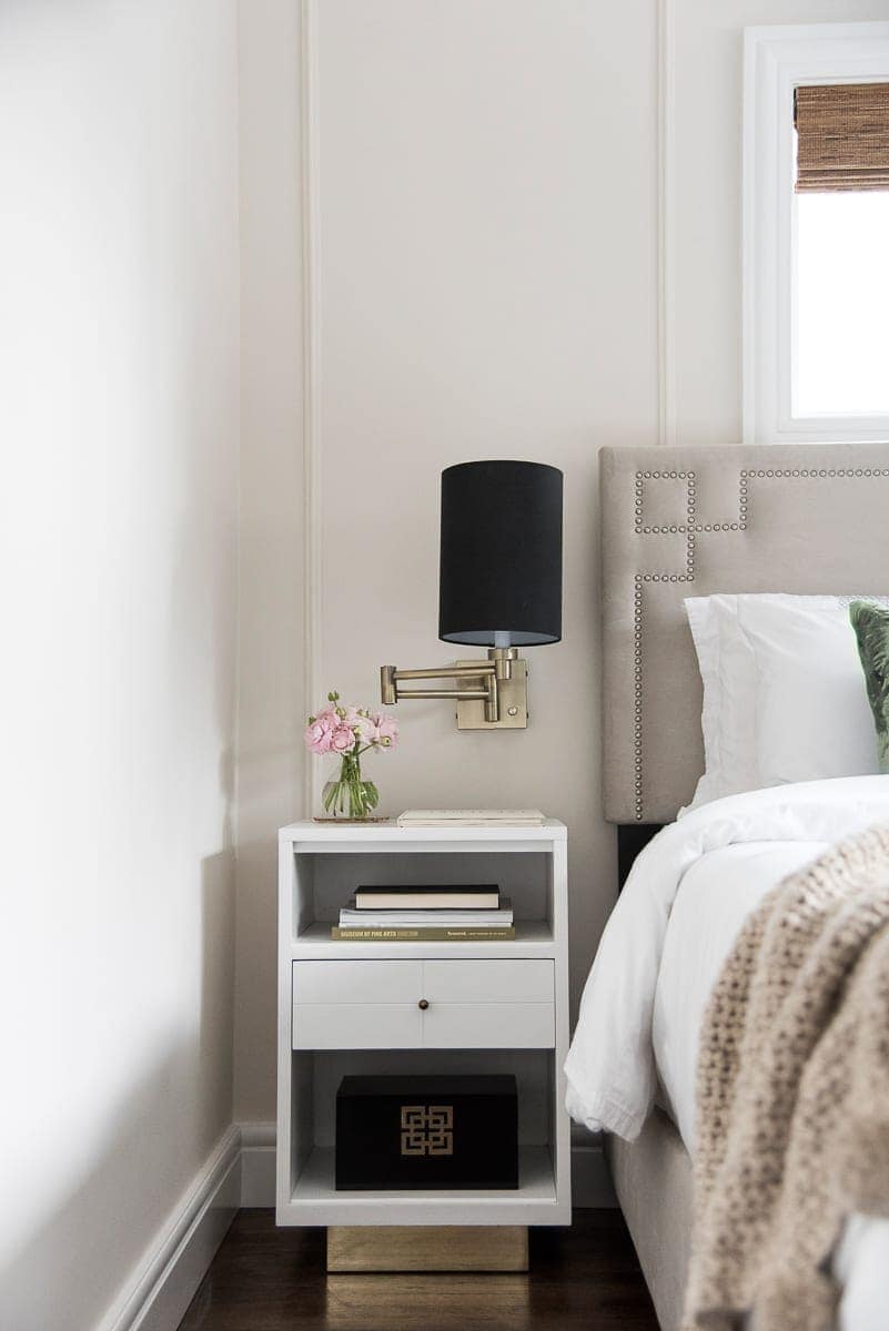 A white nightstand with gold and black sconces. 