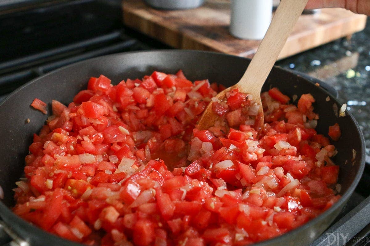 Adding chopped tomatoes to the onion and garlic mixture in a large skillet. 