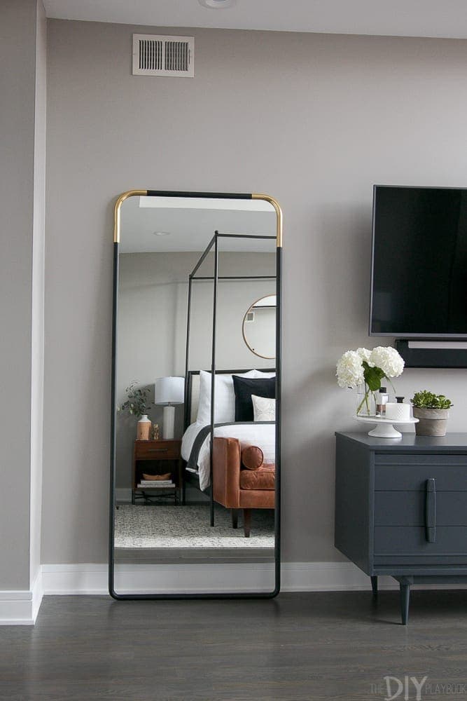 A master bedroom with a black and gold full-length mirror. 