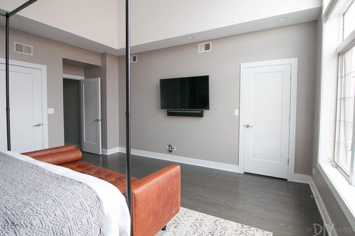 Wall opposite the bed with a mounted TV and the master bedroom entryway and bathroom door. 