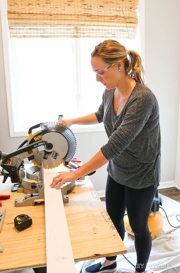 Casey in safety goggles using the DeWalt miter saw to cut wood for the guest room. 