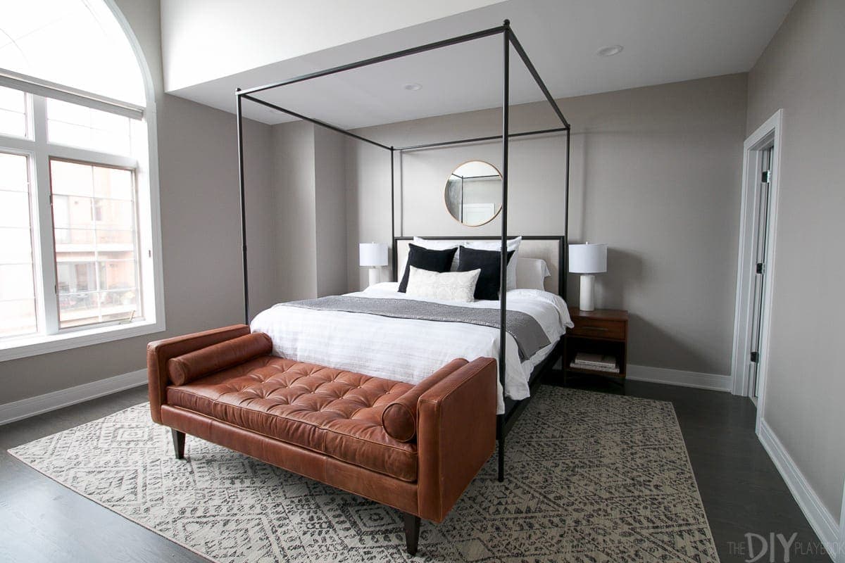 A modern master bedroom design; gray color scheme, queen size bed with white, gray and black linens, and a large gray area rug. 