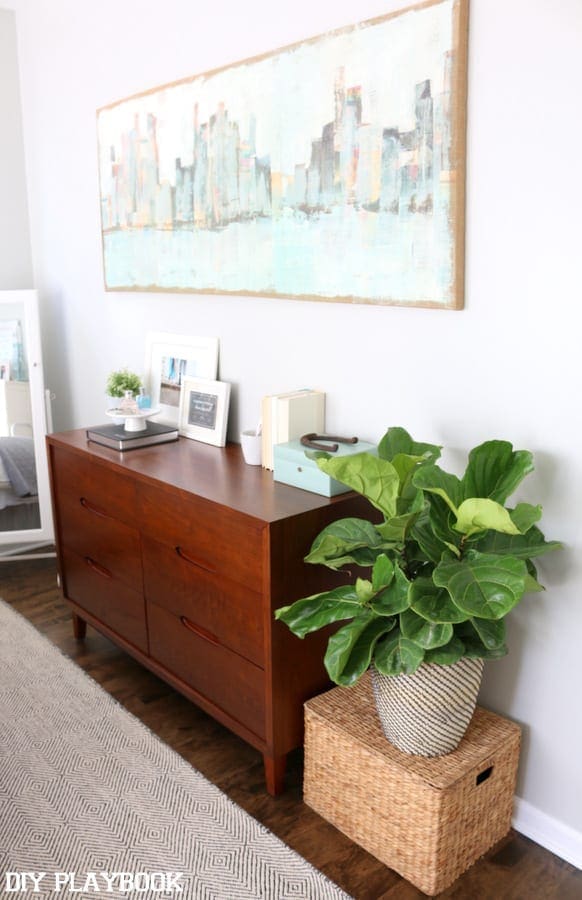 Dresser with herringbone rug and skyline painting. 