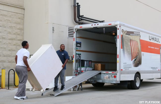 Movers work together to load a dresser into the U-Haul. 