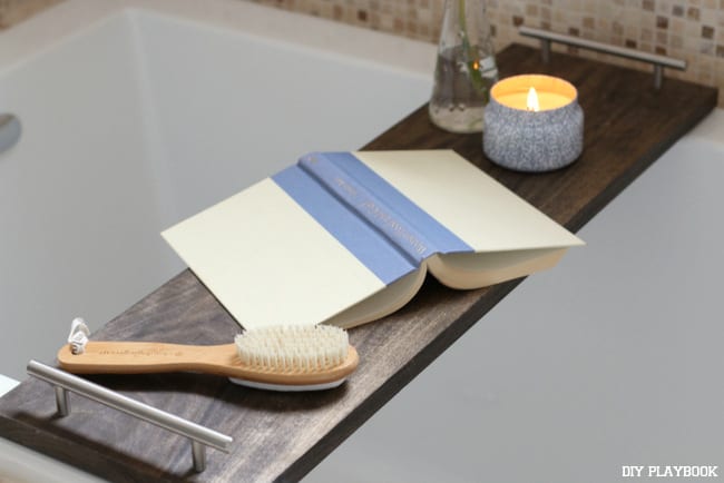 A candle, a book, and tray, all set for a relaxing bath