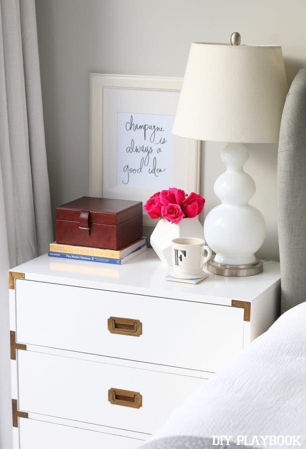 White nightstand with bright pink roses and champagne graphic art. 