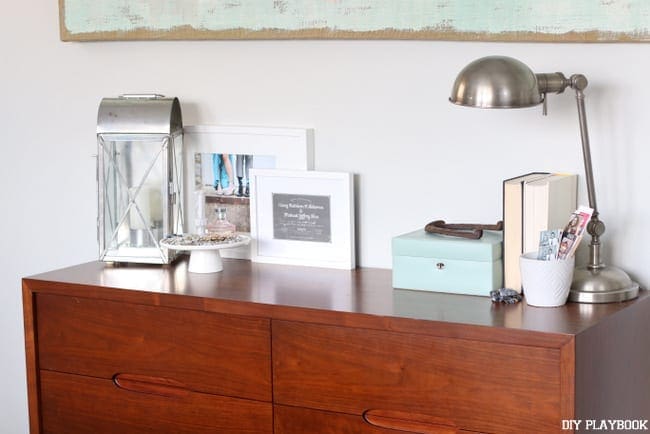 Dresser with silver lamps and white photo frames. 