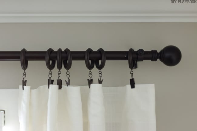 Curtain rod with brown rings and a cream colored curtain. 