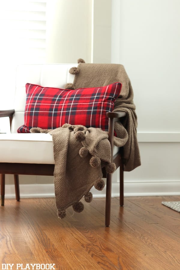 Plaid pillow on a mid century modern white chair with brown arms. 